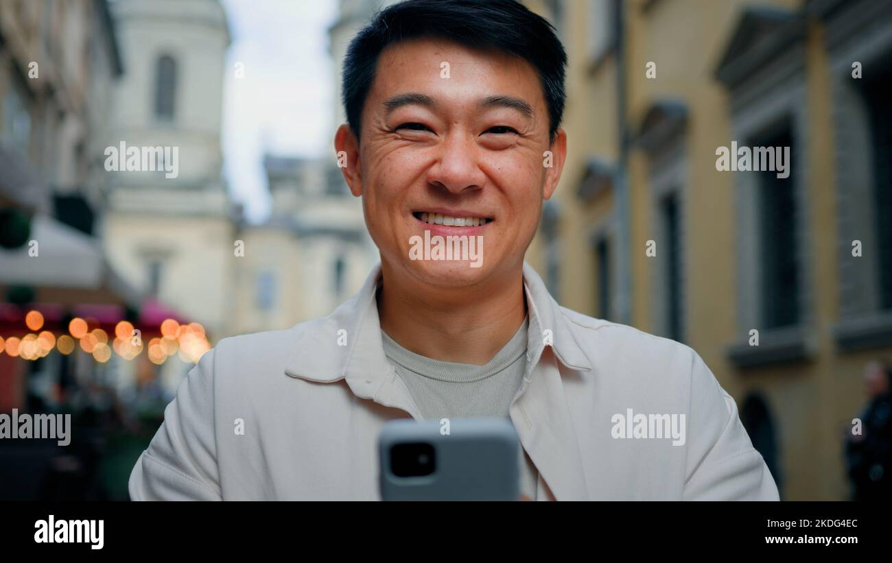 Satisfied man customer client standing outdoors holding mobile phone looking at camera enjoys internet shopping on smartphone in online store joyful Stock Photo