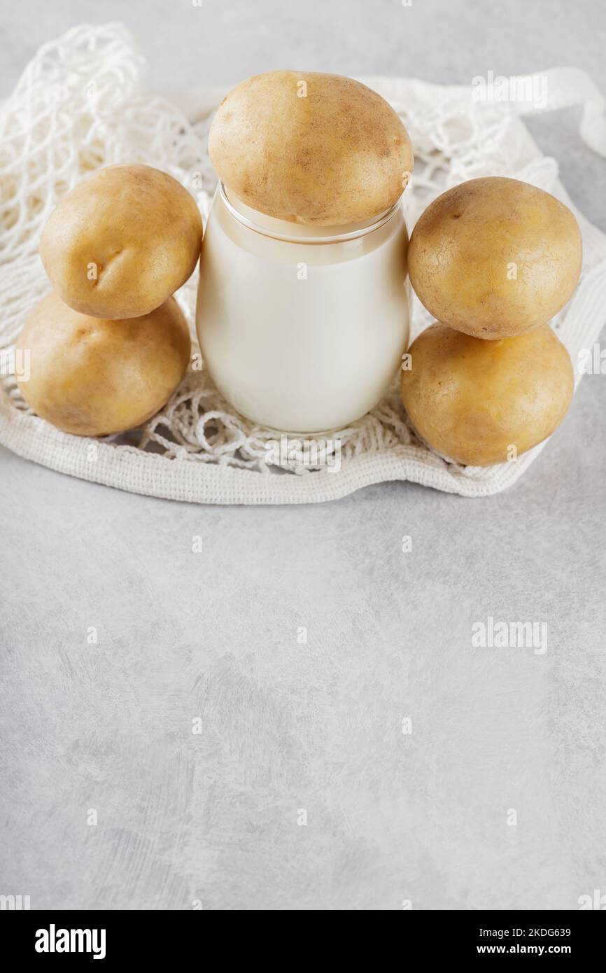 Potato milk and raw potatoes in a mesh bag. Alternative non dairy drink and ingredients on gray background. Allergens free and zero waste concept. Top Stock Photo