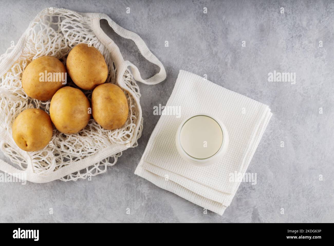 Potato milk and raw potatoes in a mesh bag. Alternative non dairy drink and ingredients on gray background. Allergens free and zero waste concept. Top Stock Photo