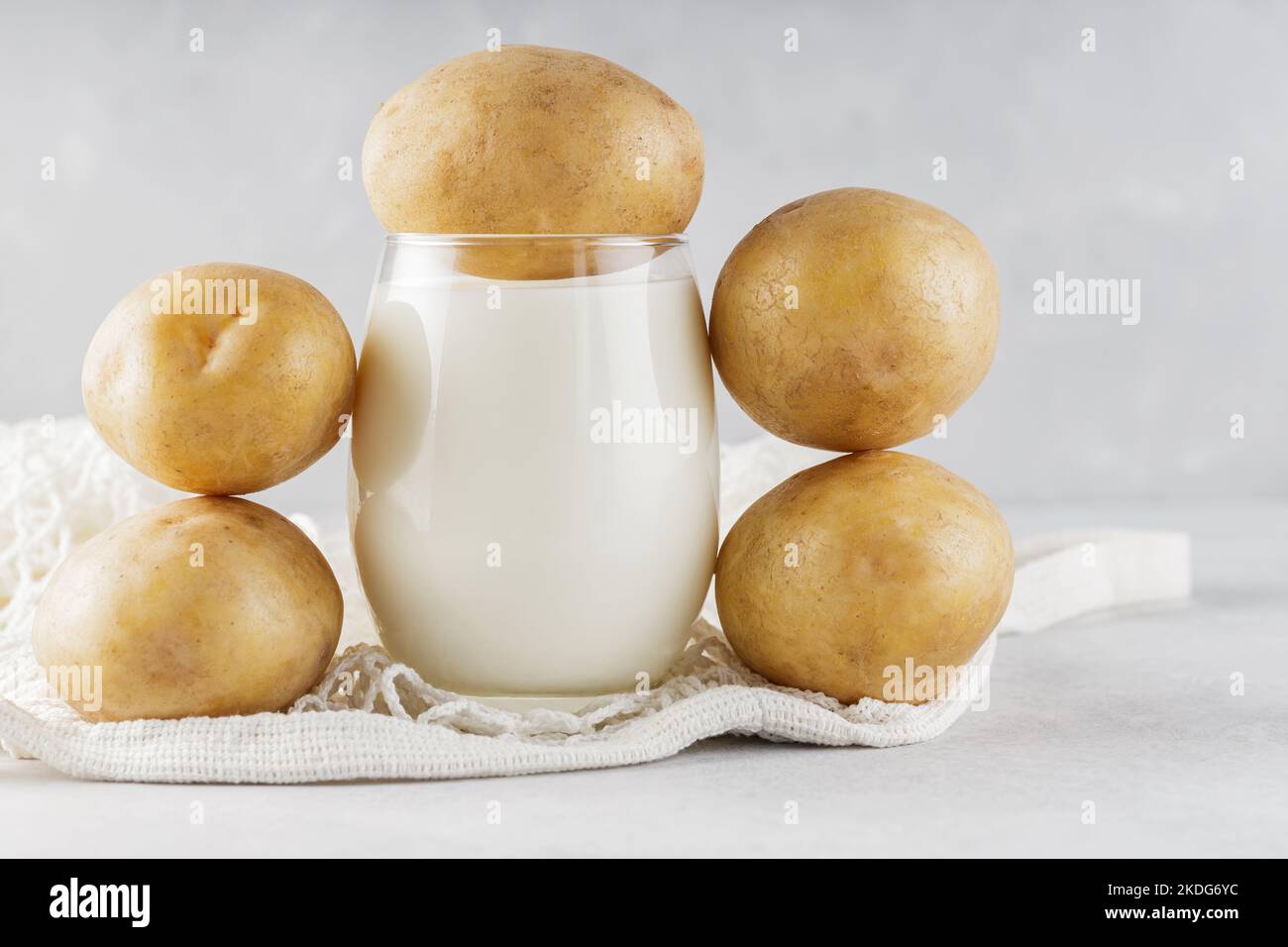 Alternative potato milk in glass and potatoes. Alternative non dairy drink and string bag. Vegan potato milk and sustainable lifestyle concept Stock Photo