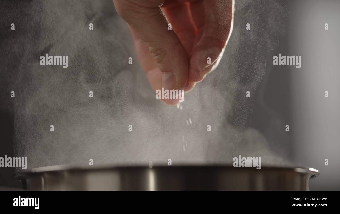man adding salt to boiling water in saucepan with strong backlight