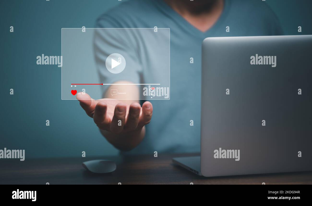Young man using laptop computer with hand holding virtual playing video streaming screen icon, future screen technology concept. Stock Photo