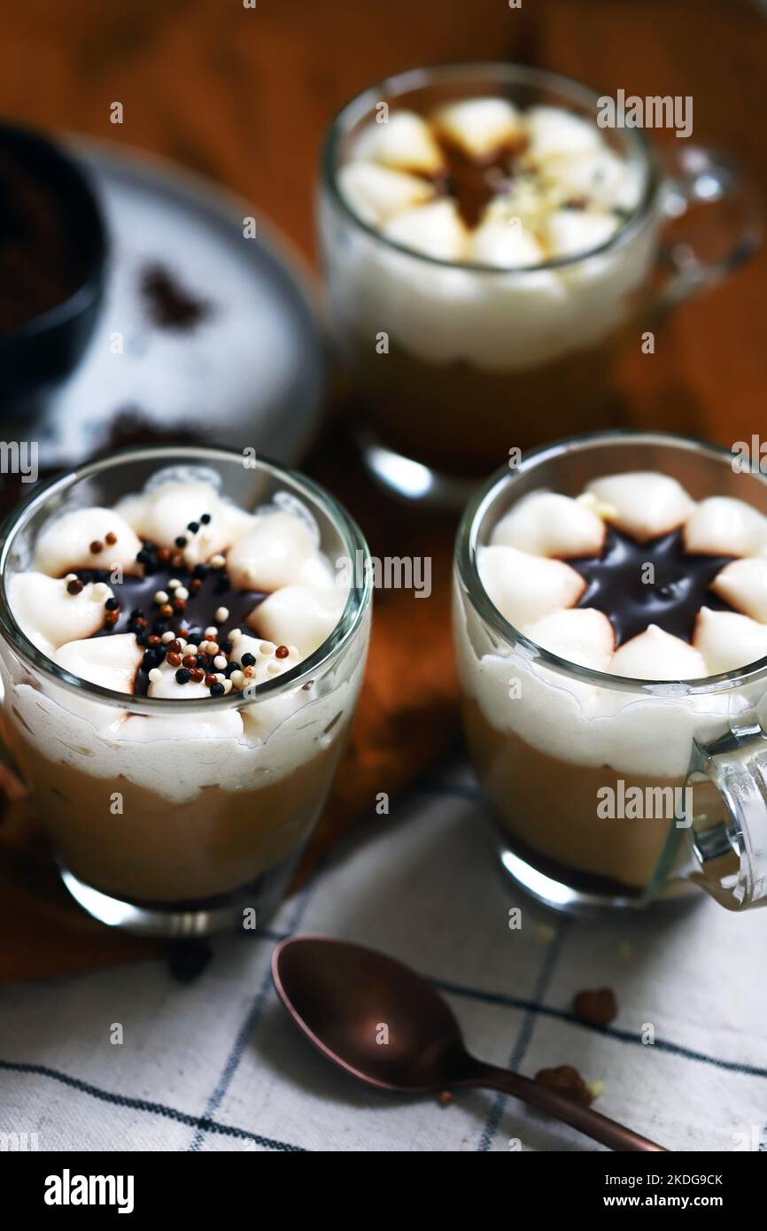 Small mugs with a three-layer coffee-caramel dessert. Delicious pudding in glass cups. Stock Photo