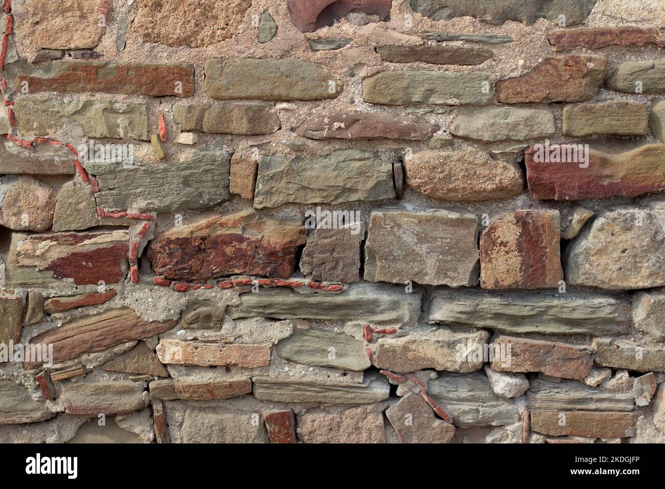 Old stone wall made of various square natural stones in beige, ocher, red and brown. Stone wall texture background  Stock Photo