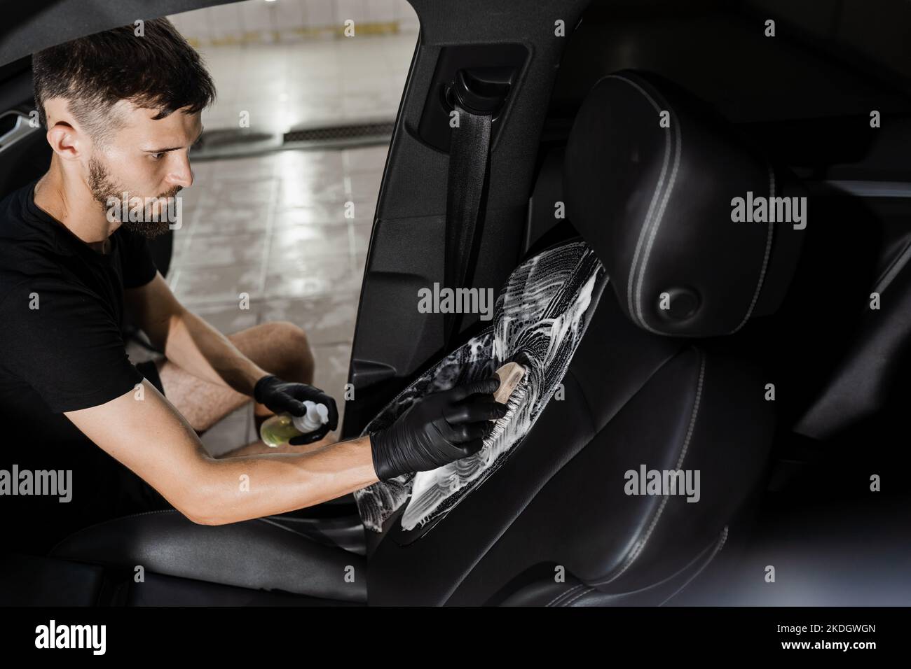 Process of foam and detergent cleaning leather seat using brush. Worker