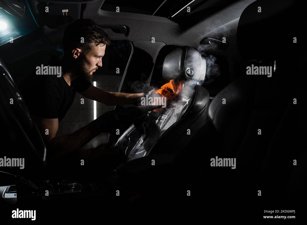 Process of steam cleaning leather seat in car. Worker in auto cleaning
