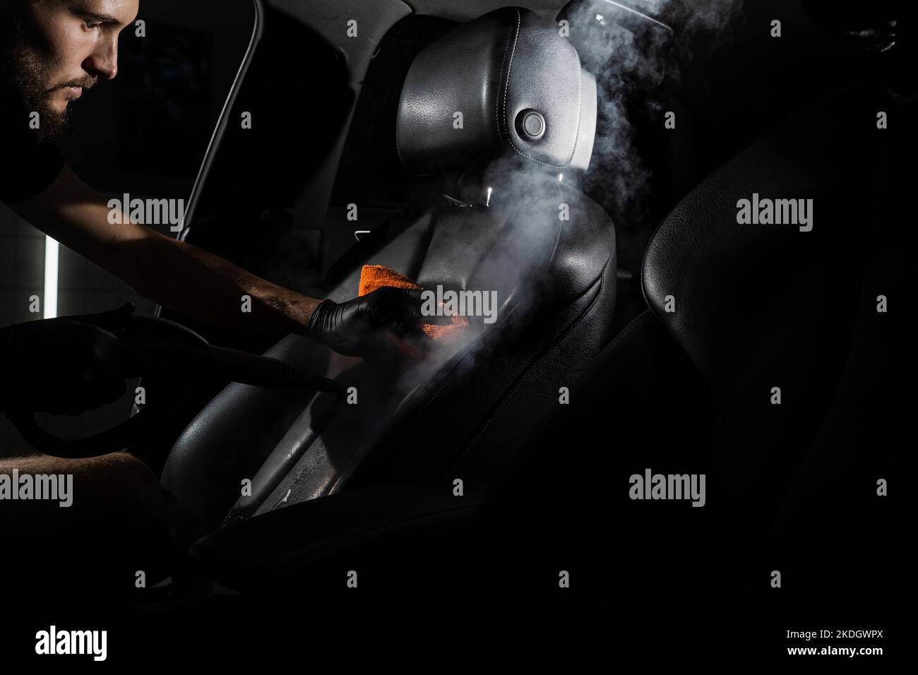 Process of steam cleaning leather seat in car. Worker in auto cleaning