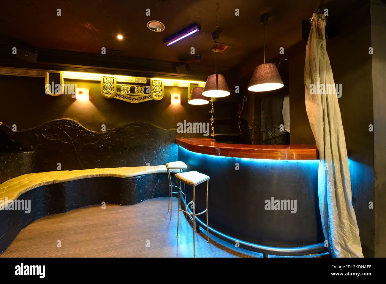 Disco room with illuminated staircase, tiers with gold cushions and black walls and ceilings and bar with blue led lights and mahogany wood countertop Stock Photo