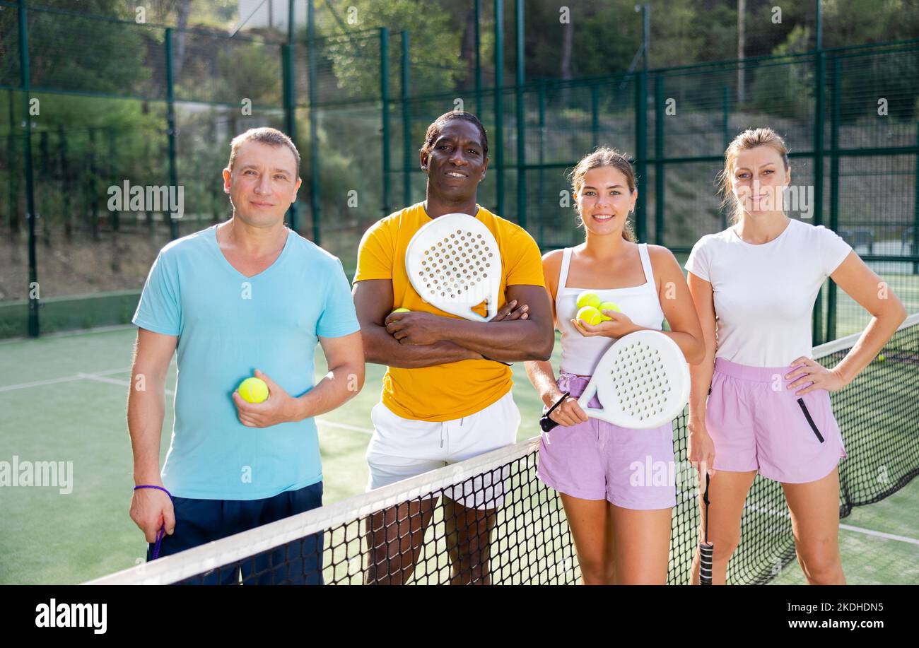 Cheerful young and adult men and women padel tennis players on court Stock Photo