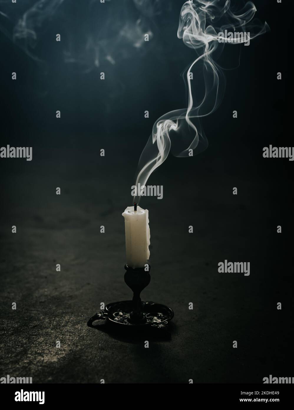 Smoke coming from a blown out candle on the floor of a dark room. Stock Photo