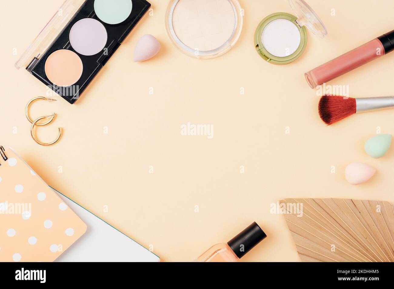 Frame made of cosmetic makeup and accessories with notepad and palm leaf on beige background. Top view, flat lay. Stock Photo