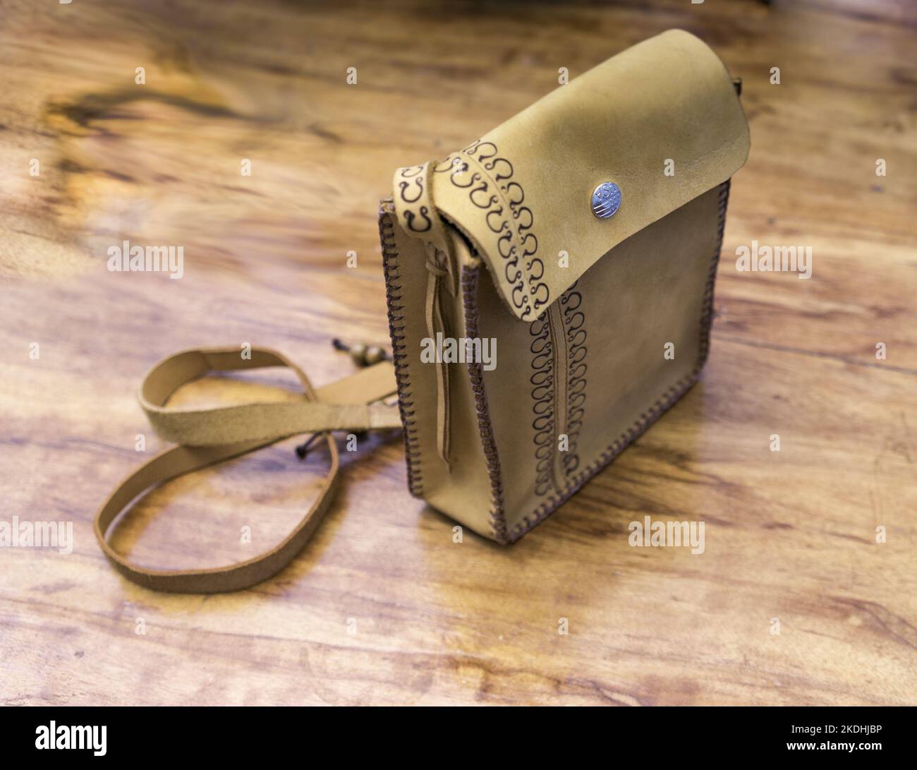 Handmade purse wtih shoulder strap coiled behind it standing upright on a wooden table. Stock Photo