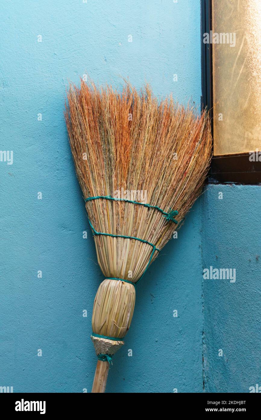 A handmade broom leans against a blue wall near a window in Jinotega, Nicaragua.  Typical of locally made brooms. Stock Photo