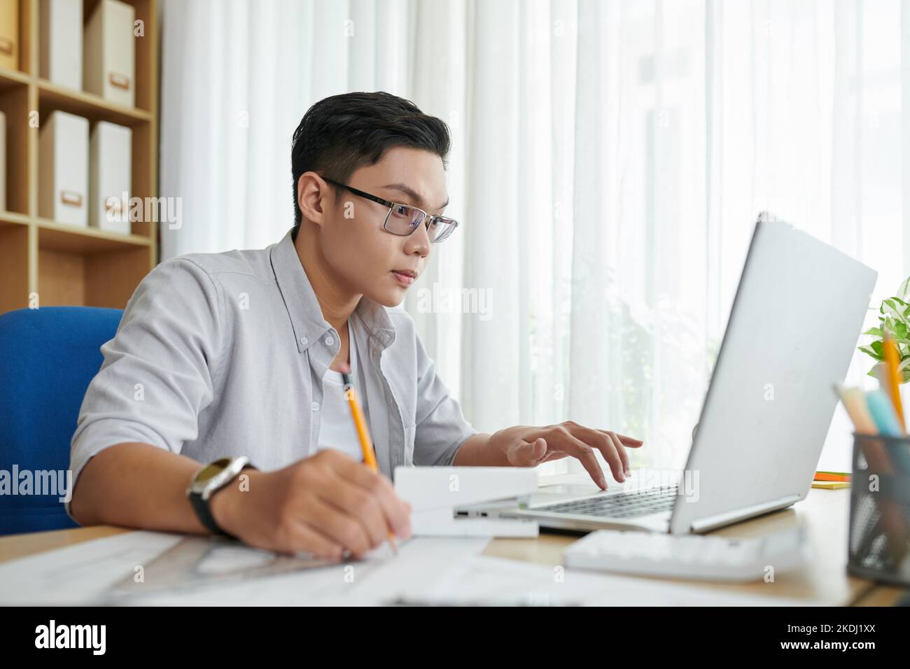Young architect reading e-mail from client and taking notes in planner Stock Photo