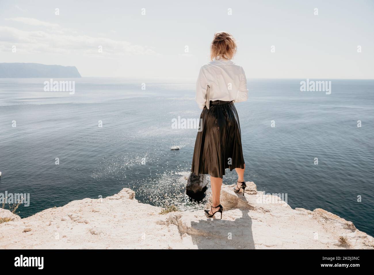 Digital nomad, Business woman working on laptop by the sea. Pretty lady typing on computer by the sea at sunset, makes a business transaction online Stock Photo