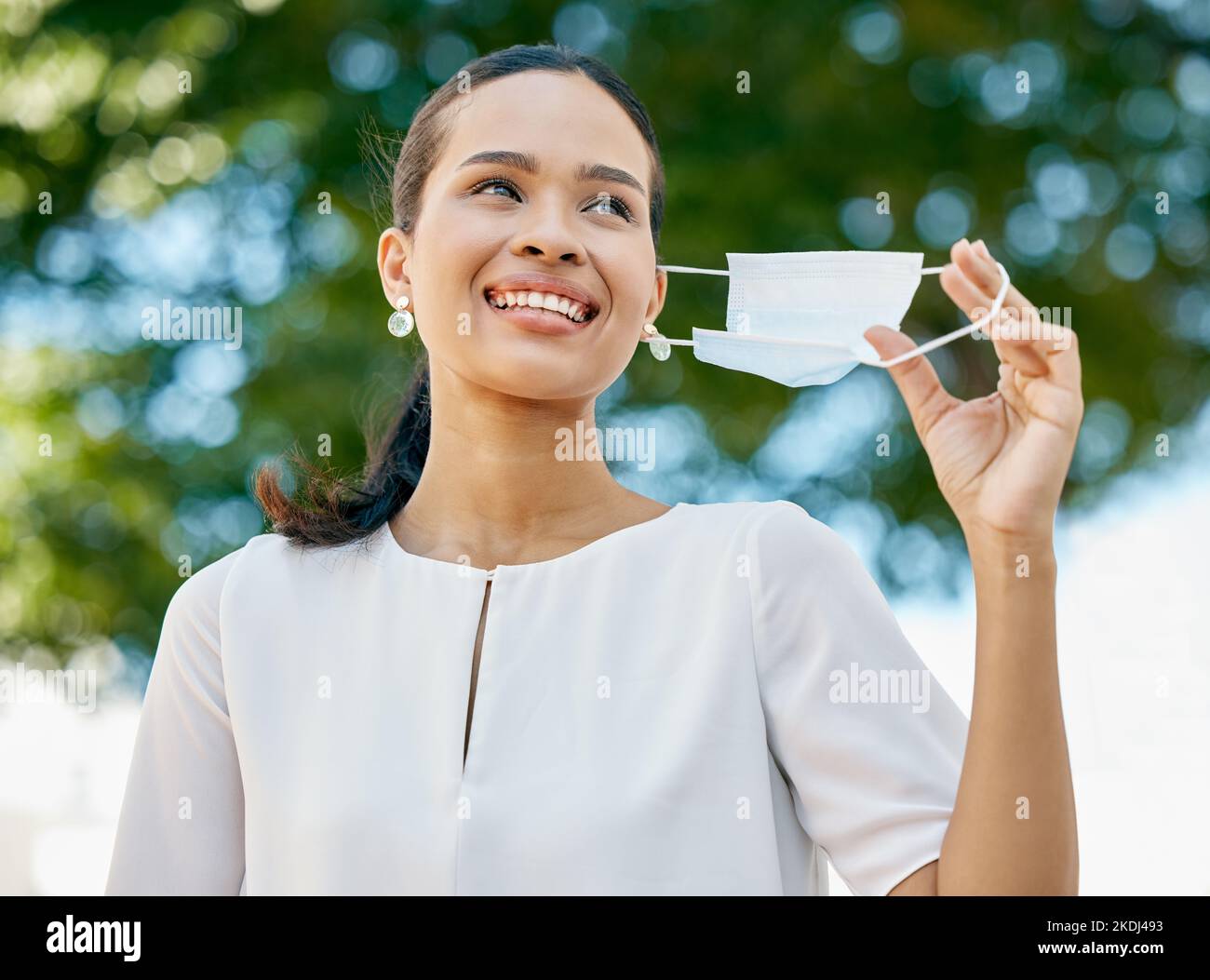 Covid, woman in park taking off face mask and celebrate end of the pandemic with smile. Trees, fresh air and freedom from mask, happy businesswoman in Stock Photo