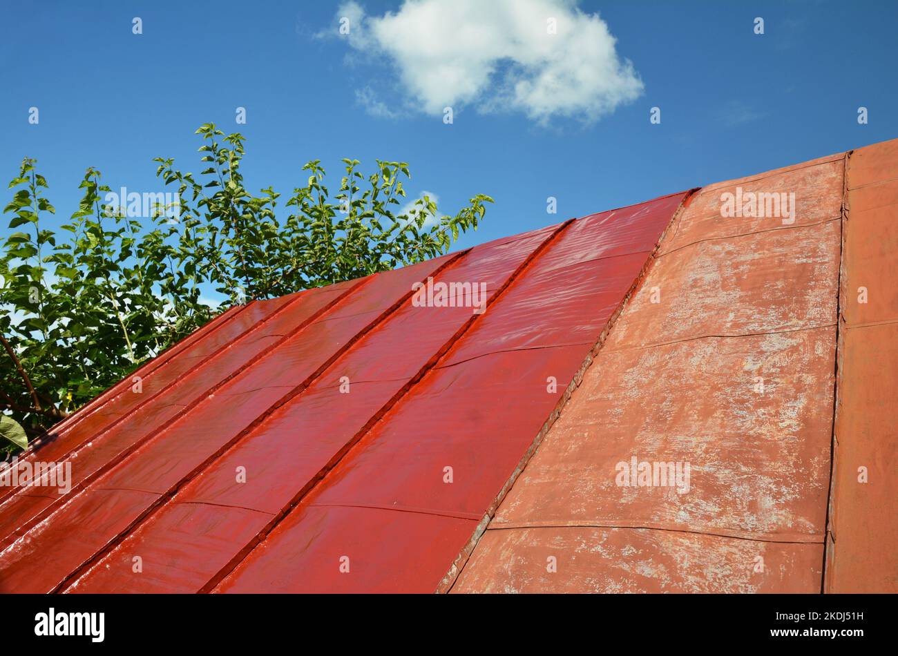 Repainting old metal roof surface. Steel roofing unfinished renovation with red paint Stock