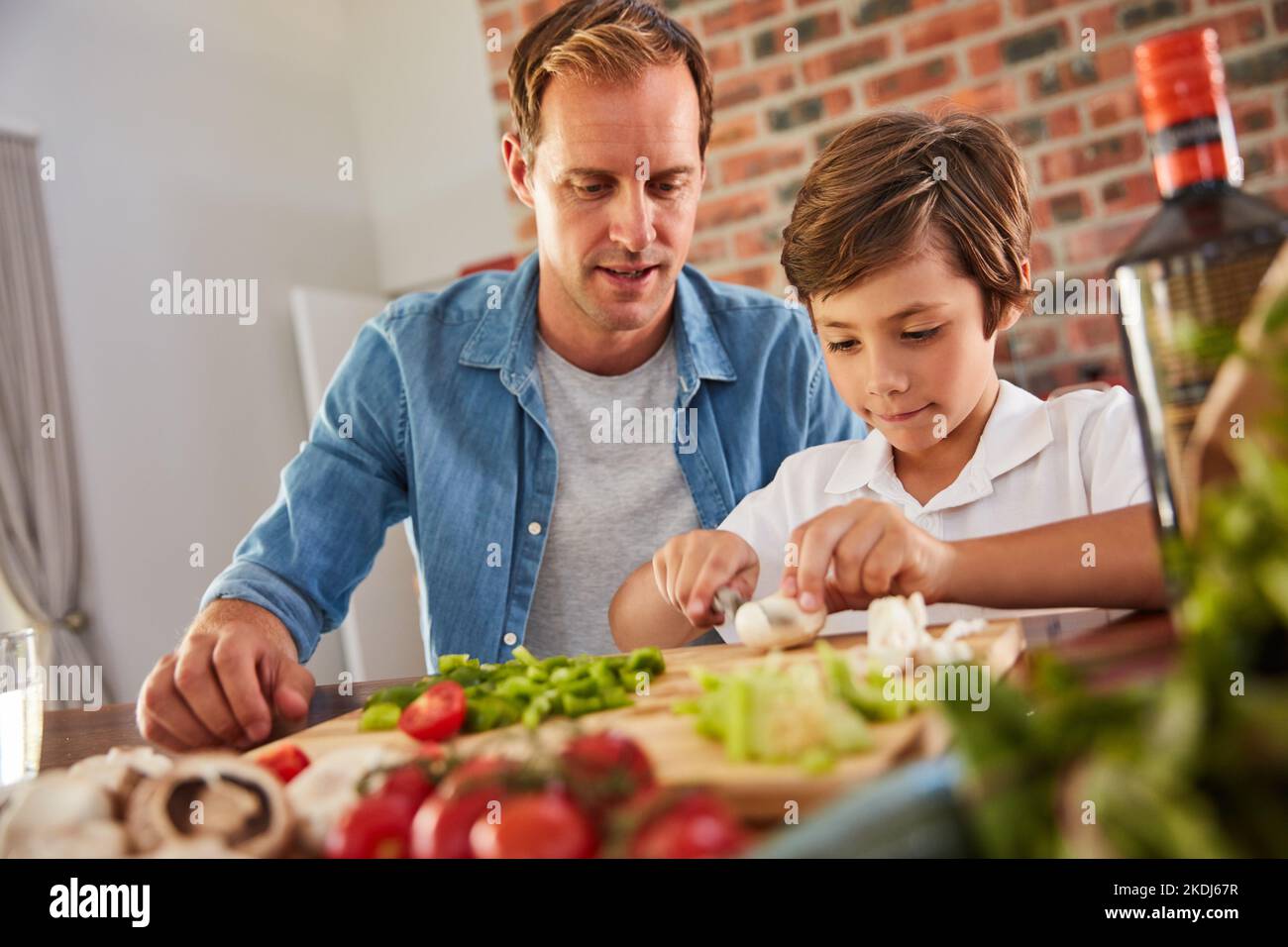 Teaching dad a thing or two in the kitchen. a father watching his little boy chop vegetables in the kitchen. Stock Photo