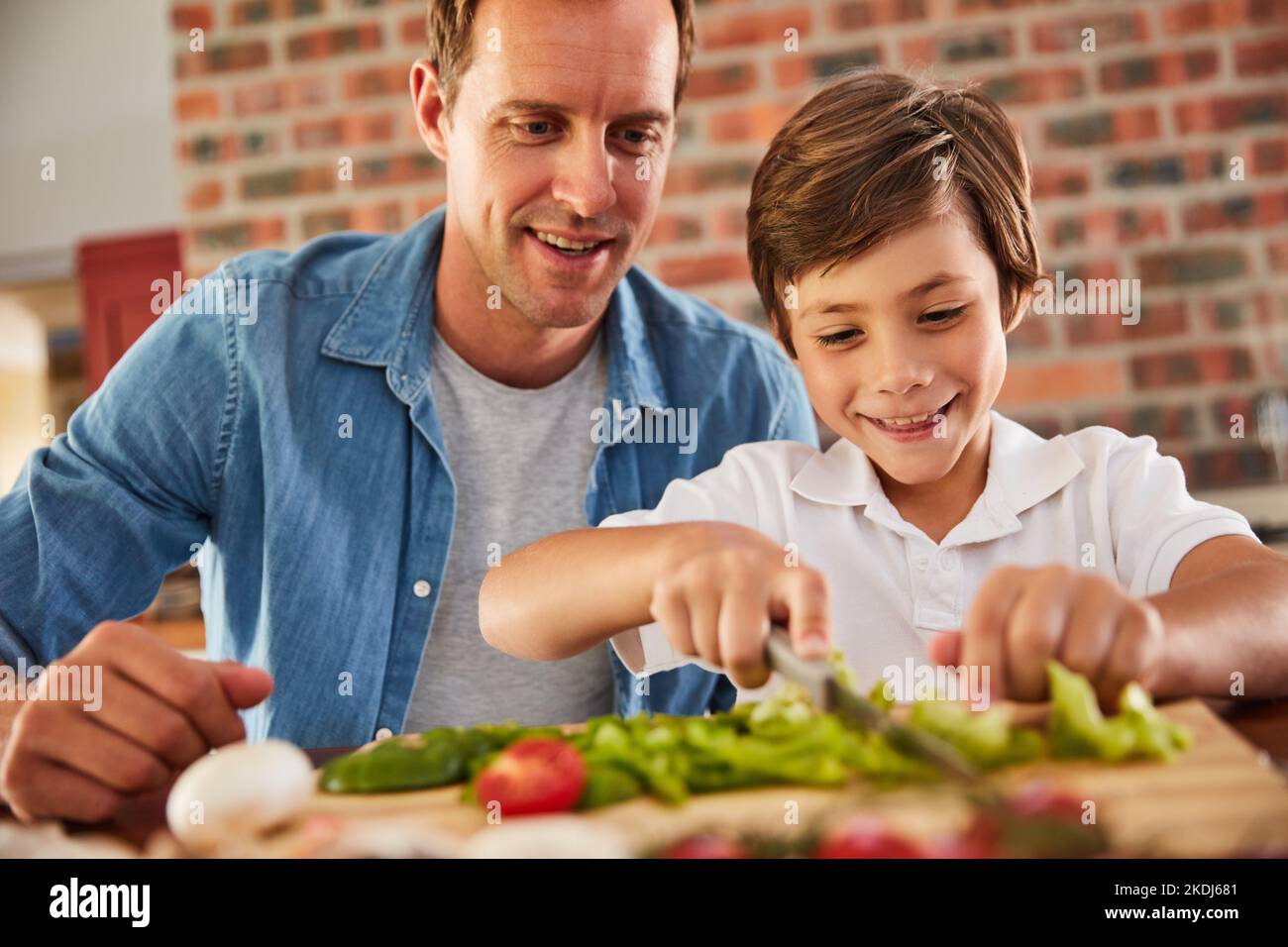 Hes a Masterchef in the making. a father watching his little boy chop vegetables in the kitchen. Stock Photo