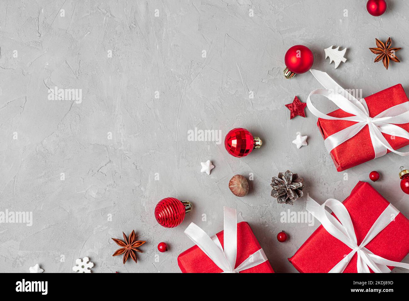 Christmas composition. Red gift boxes with holiday decorations, pine cones and nuts on gray background. Flat lay. Top view with copy space Stock Photo