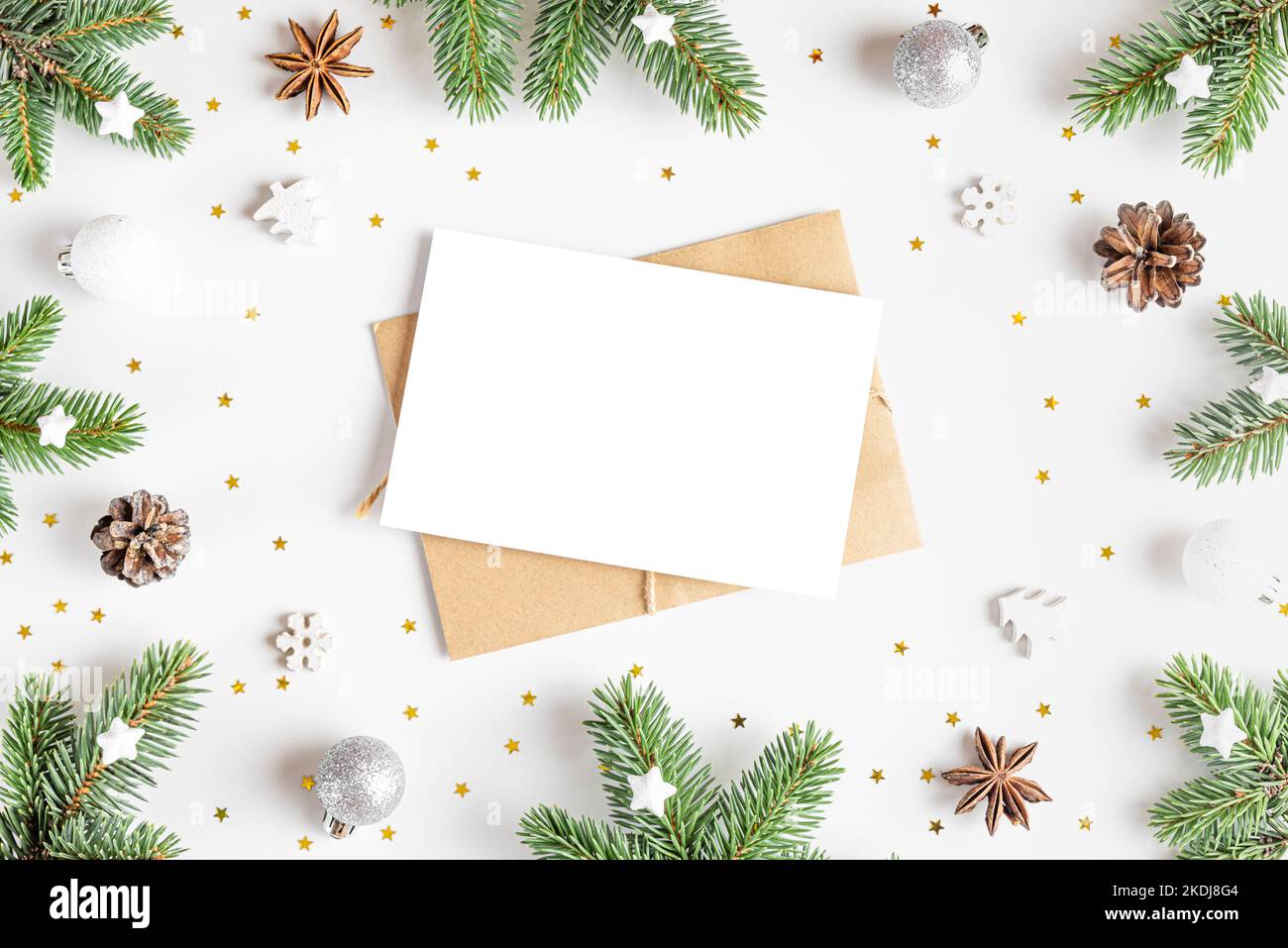 Christmas greeting card in frame made of fir tree, holiday decorations on white background. Mock up. Flat lay. Top view Stock Photo