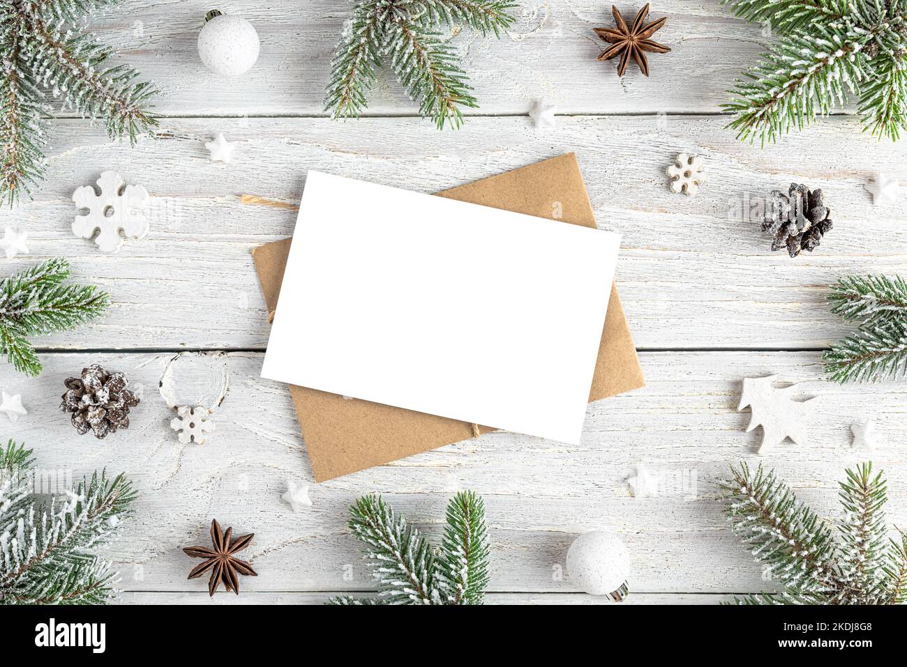 Christmas greeting card in frame made of fir tree, holiday decorations on white wooden background. Mock up. Flat lay. Top view Stock Photo