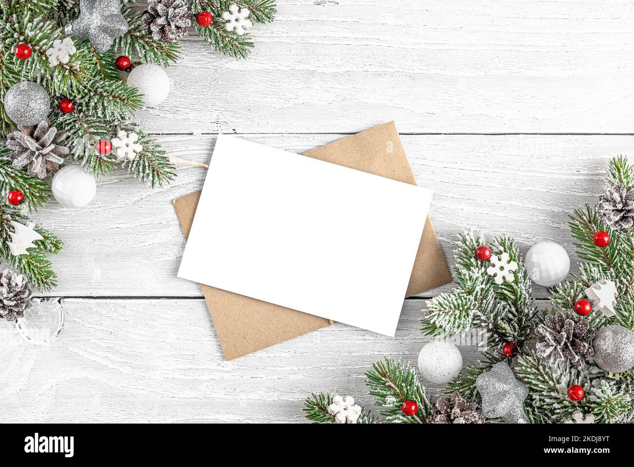 Christmas greeting card with fir tree, red holiday decorations on white wooden background. Mock up. Flat lay. Top view Stock Photo