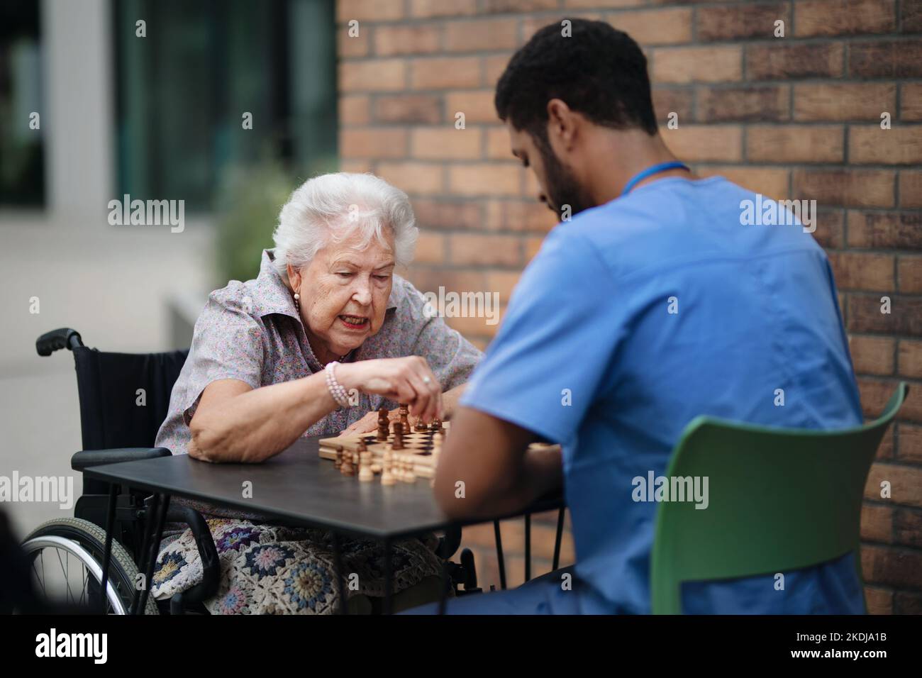 Caregiver playing chess with his client outdoor at cafe. Stock Photo