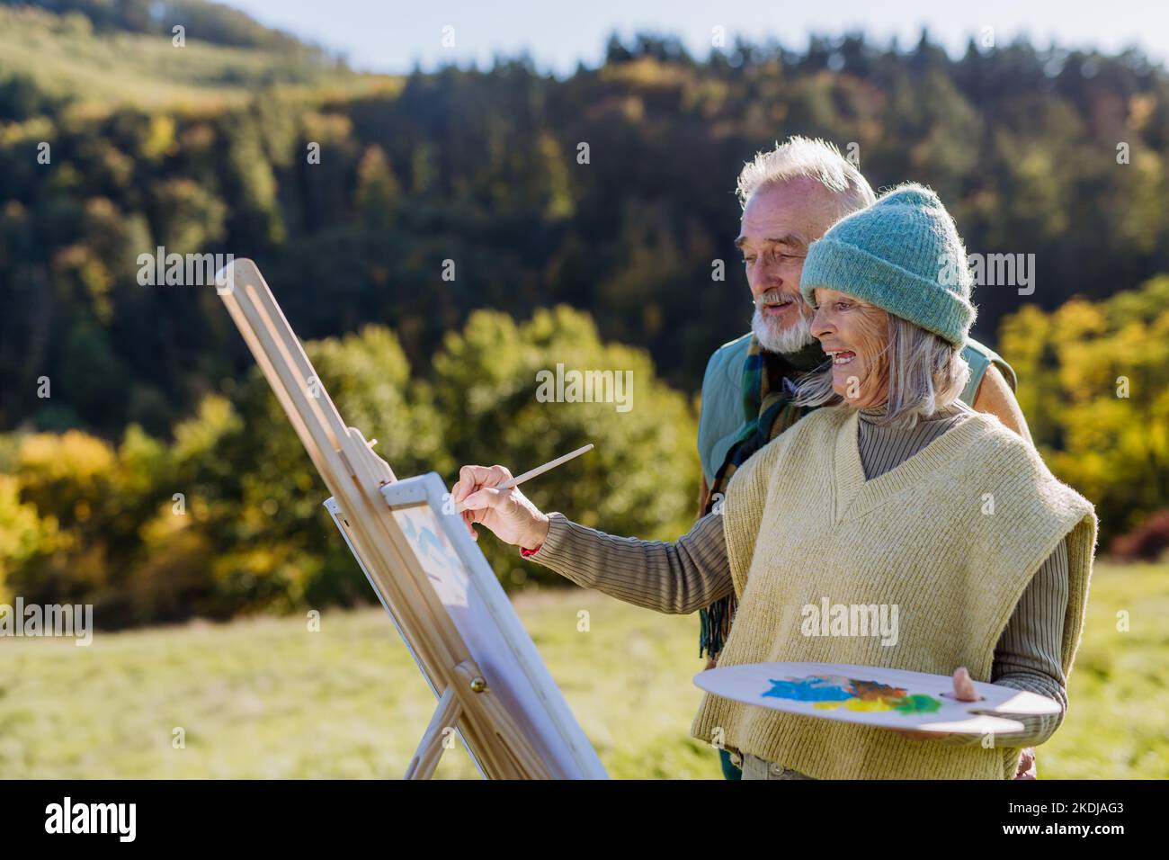 Senior couple painting together in nature, during autumn day. Stock Photo