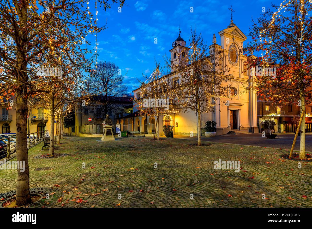 Catholic church on cobblestone town square and trees illuminated with Christmas lights in Alba, Piedmont, Northern Italy. Stock Photo