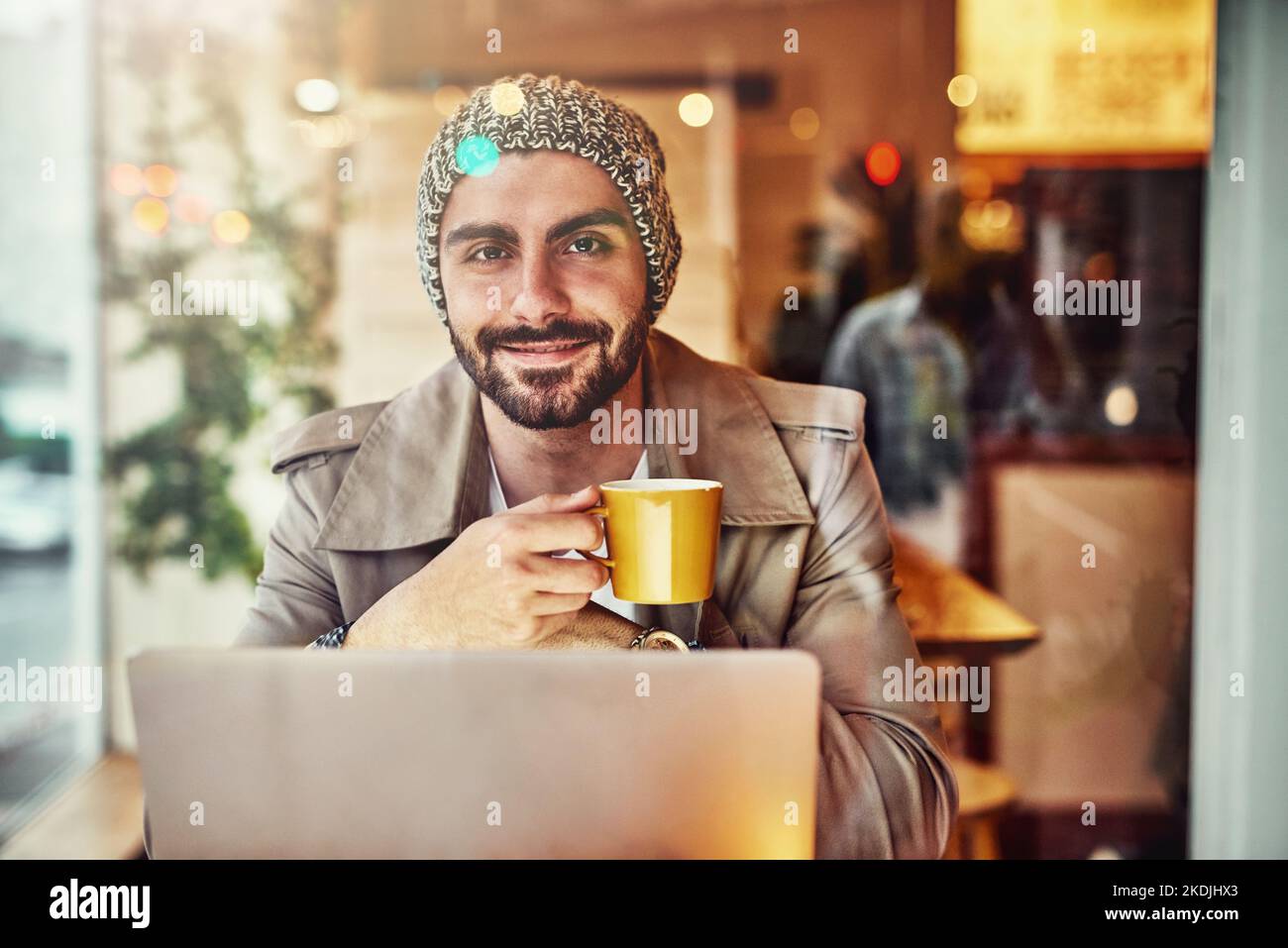 Just chilling at my local cafe. Portrait of a stylish young man smiling while drinking a coffee and using a laptop in a cafe. Stock Photo