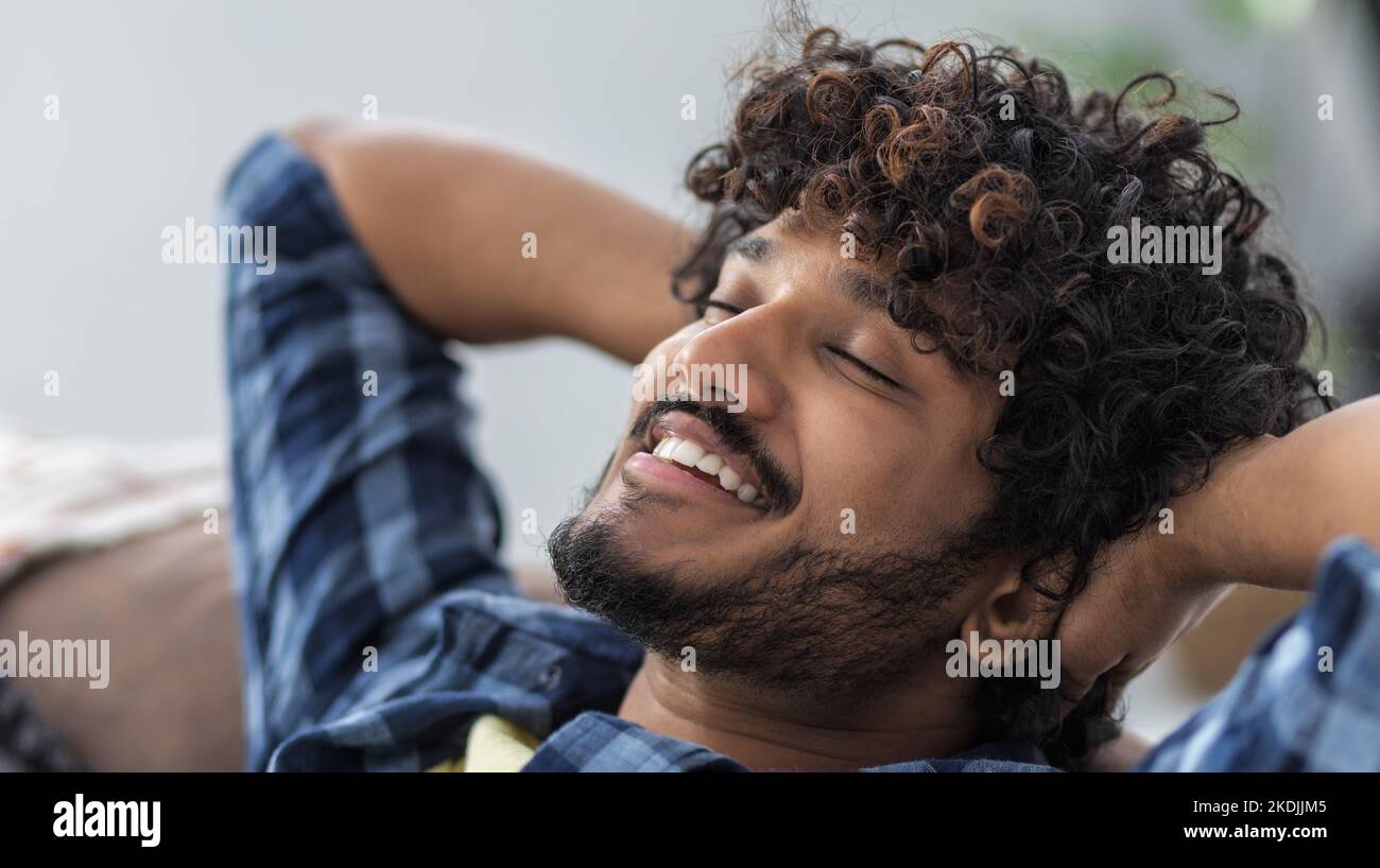 Relax at home, positive thinking. Young male throwing his hands behind his head thinks of something good Stock Photo