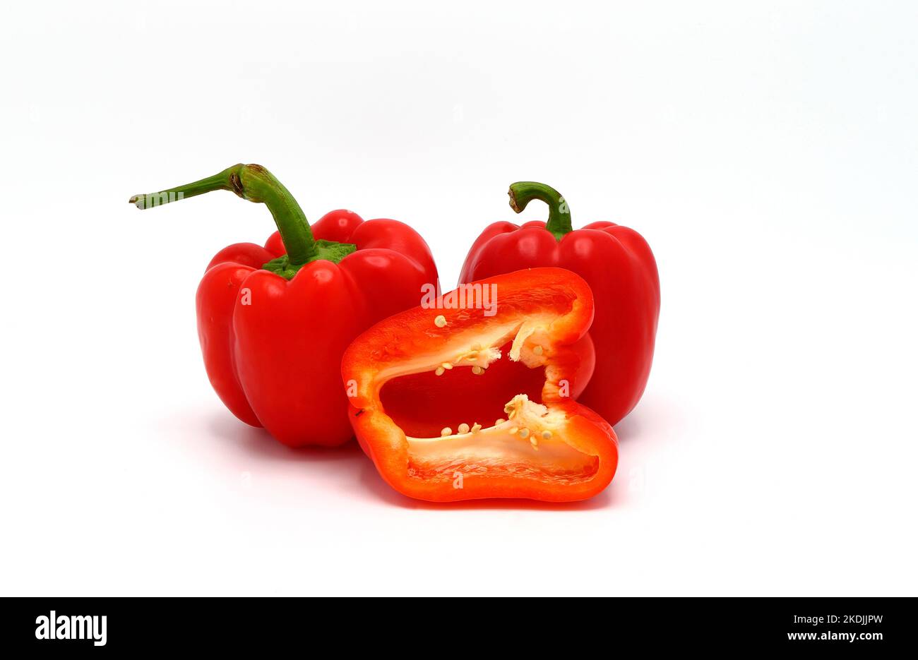 Two red ripe sweet peppers and one pepper in a cut on a light
