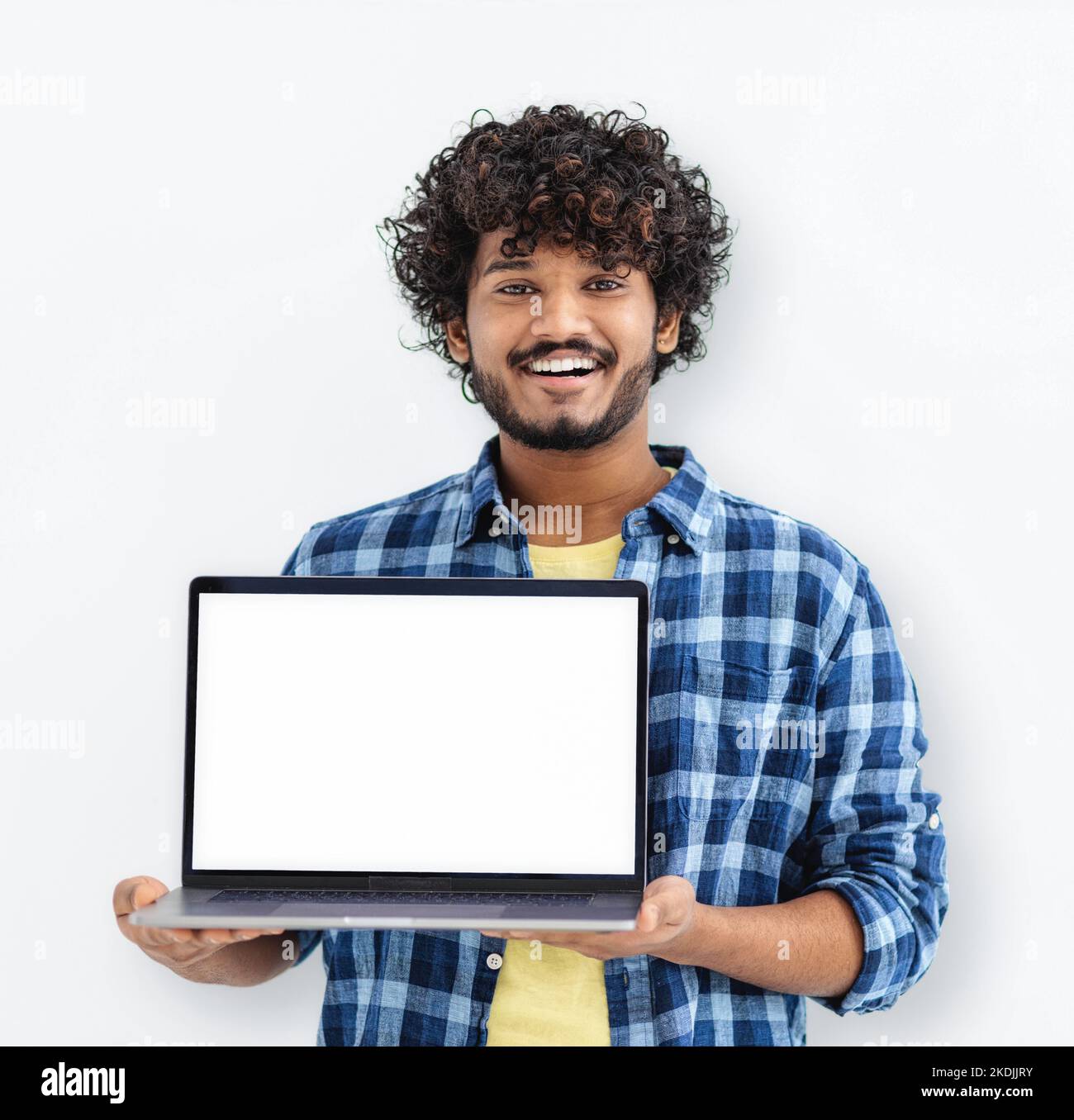 Happy Indian man student standing with open laptop with blank white mockup screen on white background Stock Photo