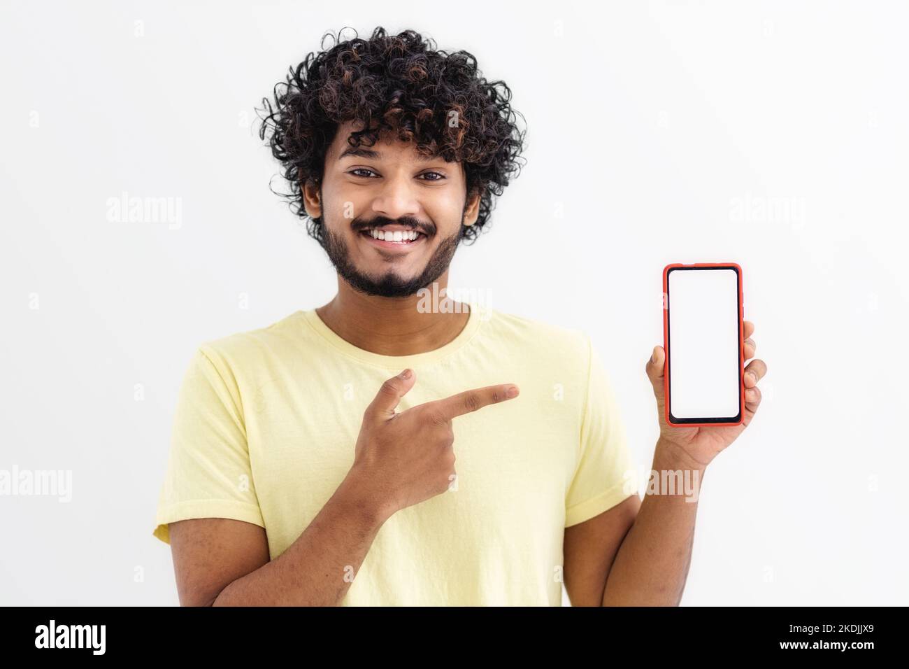 Happy Indian man student standing with mobile phone, pointing his finger at the empty screen on white background Stock Photo