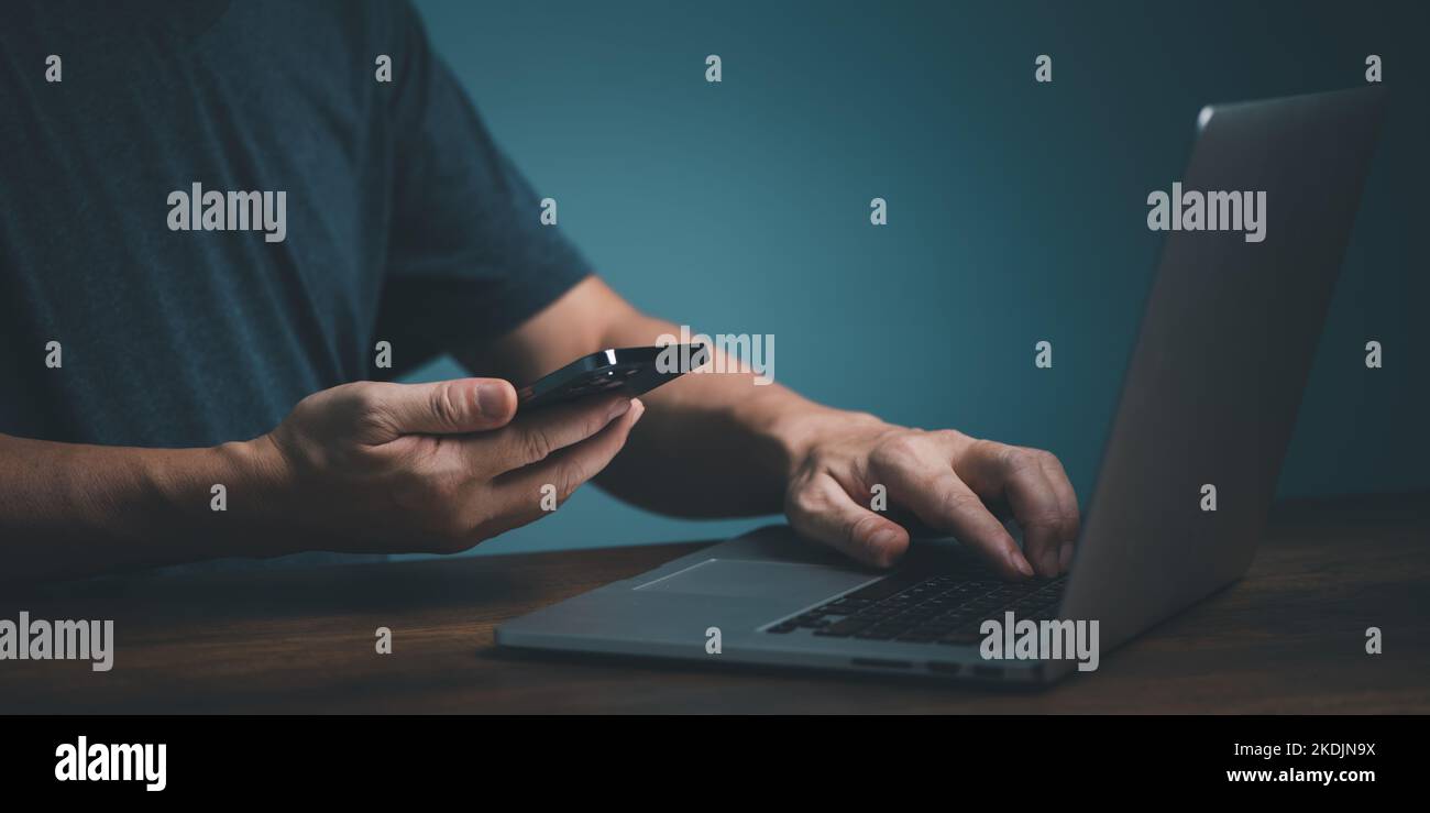 Man holding smartphone getting message with confirmation making transaction, transfer, synchronizing data via bluetooth on laptop computer. Stock Photo