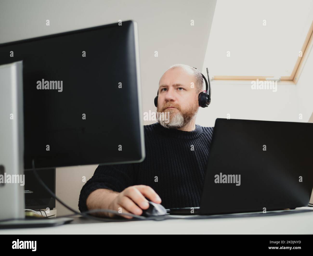 Adult man remote working on laptop and using two monitors and headphones from home Stock Photo