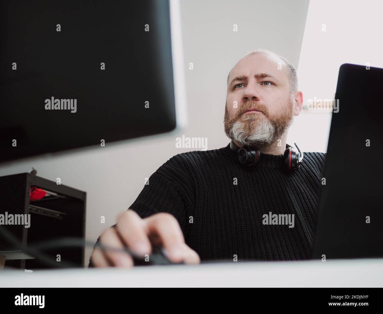 Adult focused bearded man remote working on laptop and using two monitors from home Stock Photo