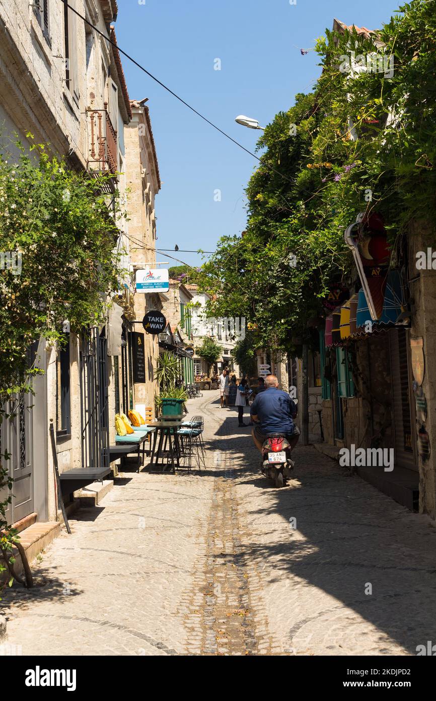 View of people walking on street and old, historical, traditional stone houses in famous, touristic Aegean town called Alacati. It is a village of Ces Stock Photo