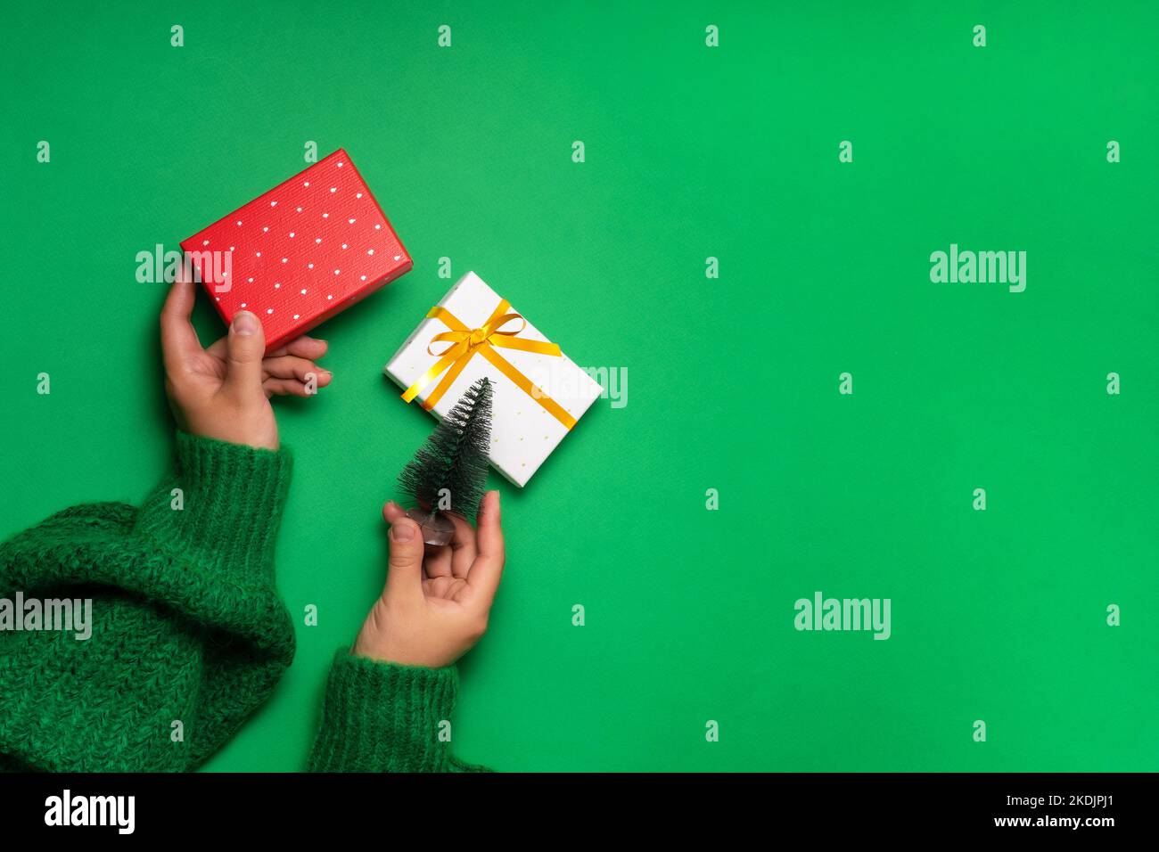 Small Christmas tree in female hands over the table, gift boxes lie