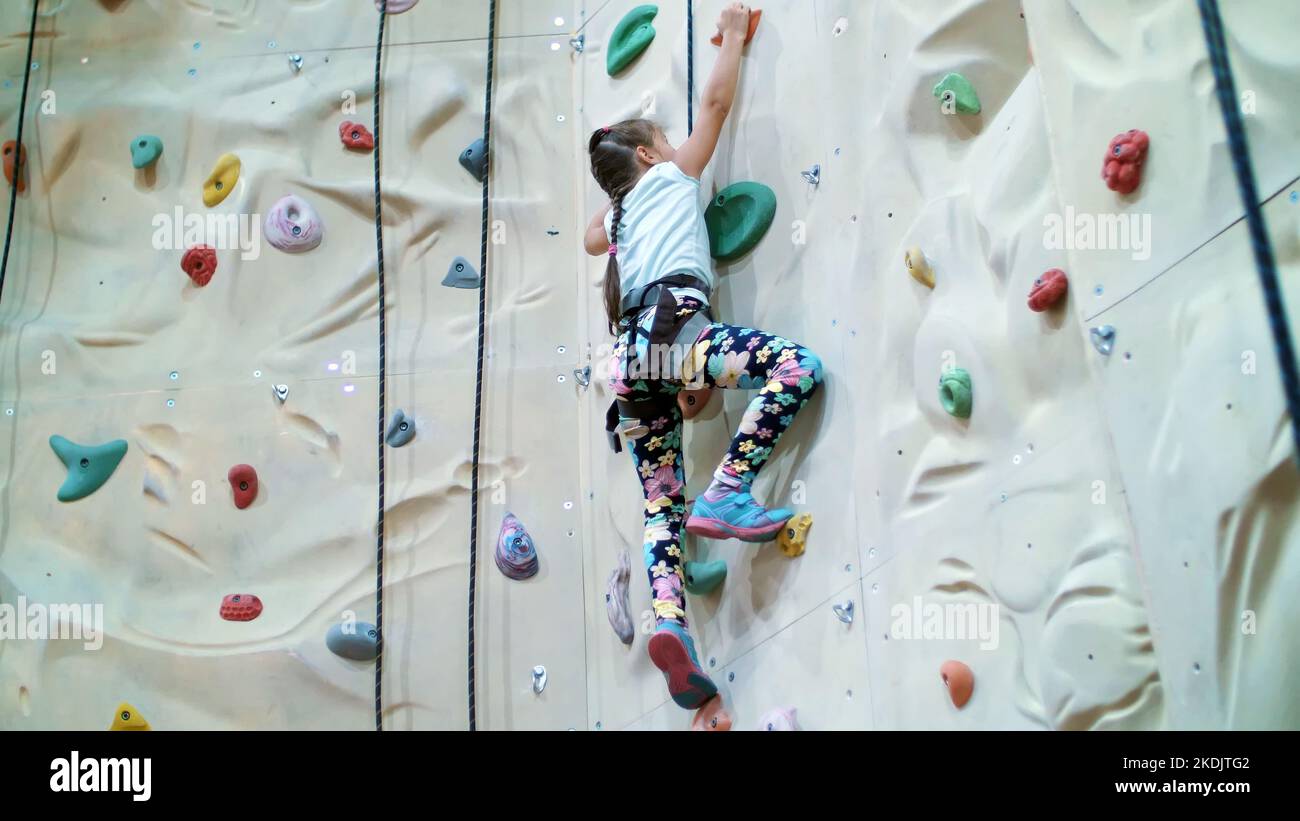 child climbs on a special wall for mountaineering. the girl of seven years in safety equipment is engaged in rock climbing on a special training vertical wall,. High quality photo Stock Photo