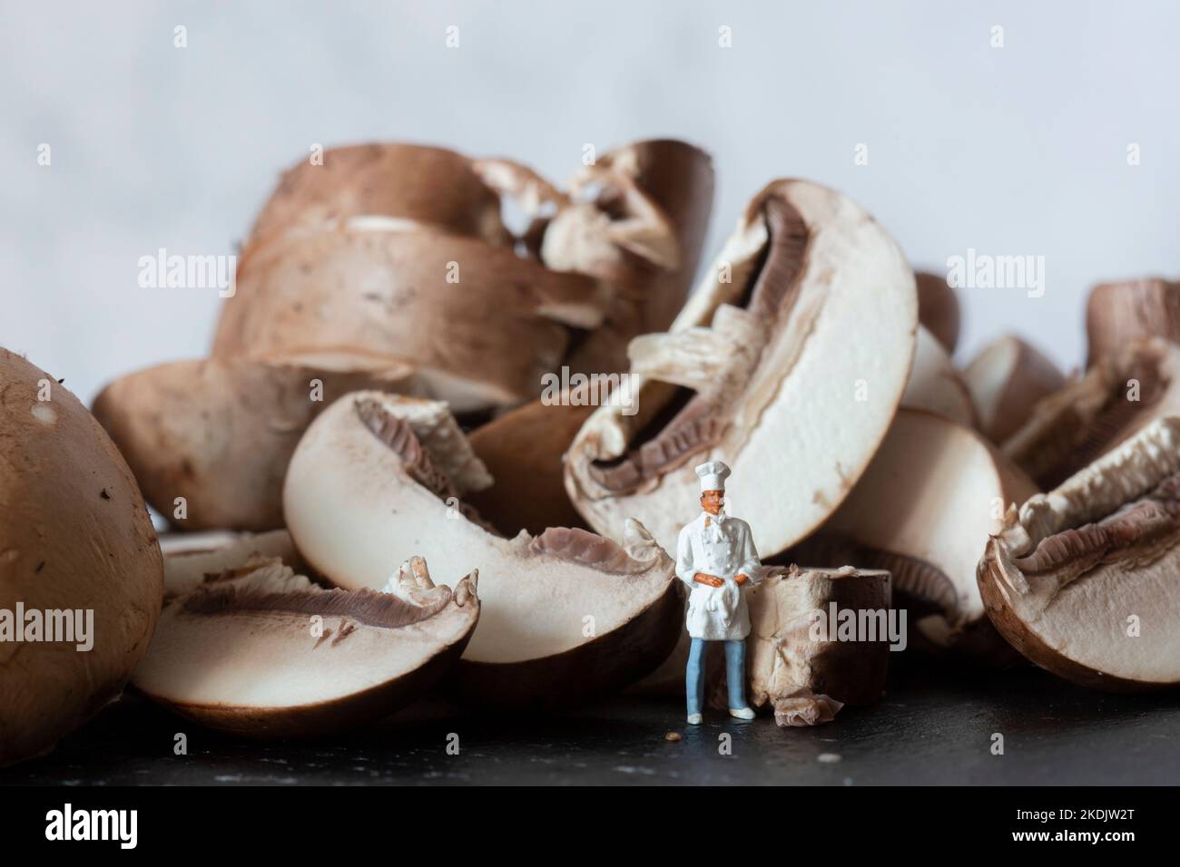 Sliced chestnut mushrooms on a slate cutting board, with a miniature scale model chef in uniform Stock Photo