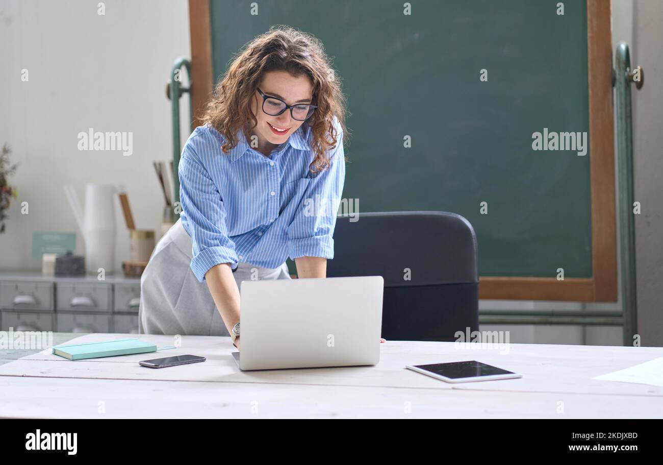 Young woman school teacher, online tutor standing at desk teaching remote class. Stock Photo