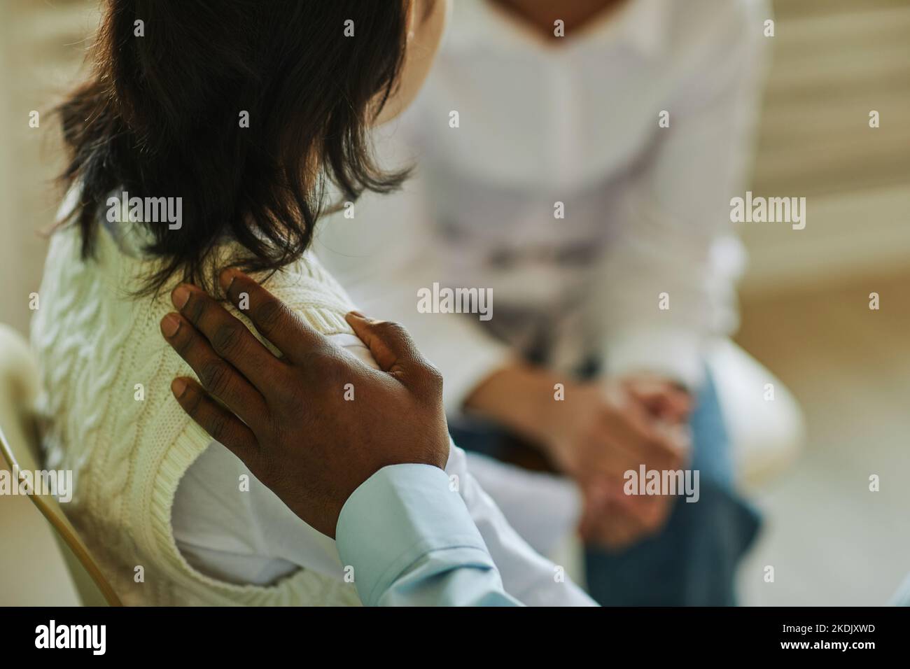 Hand of young African American man on shoulder of schoolgirl with dark long hair supporting her during psychological session Stock Photo