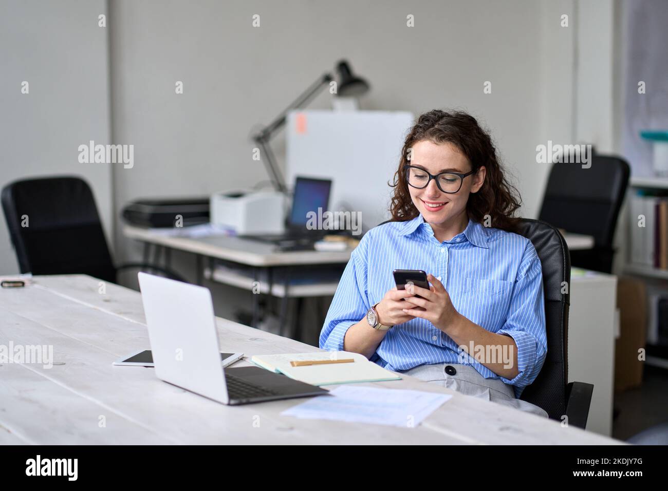 Young business woman using cellphone working in office sitting at desk. Stock Photo
