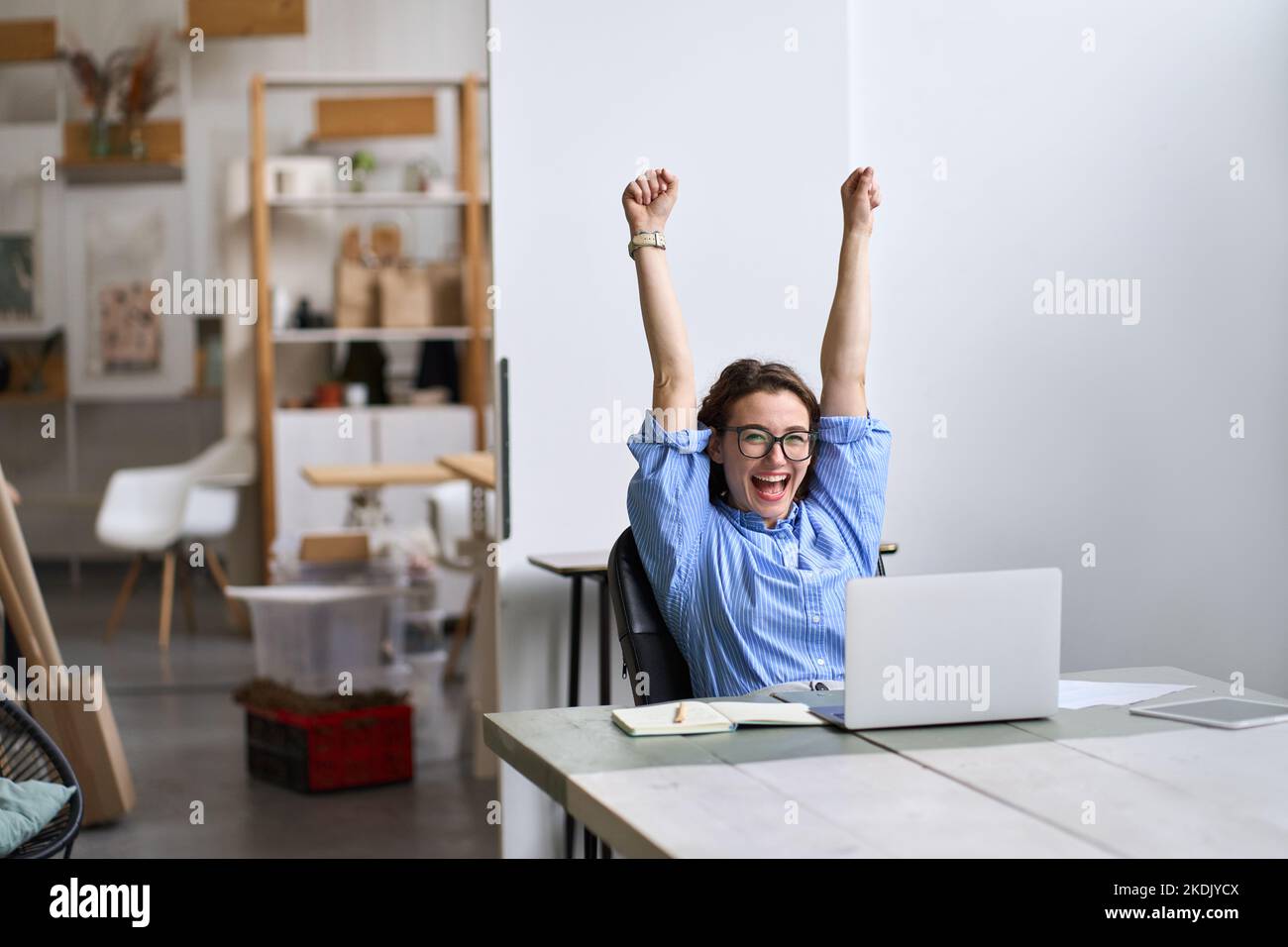 Happy excited young woman student or employee using laptop celebrating success. Stock Photo