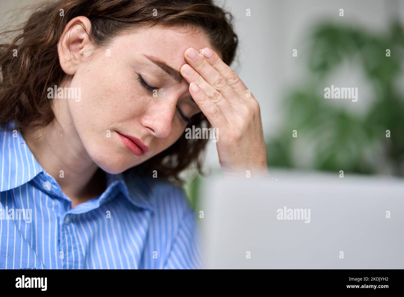 Tired young business woman touching head feeling migraine fatigue at work. Stock Photo