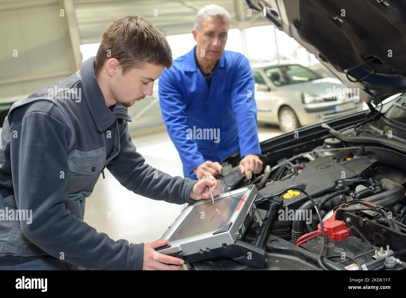 trainee testing car electronics with computer in professional garage