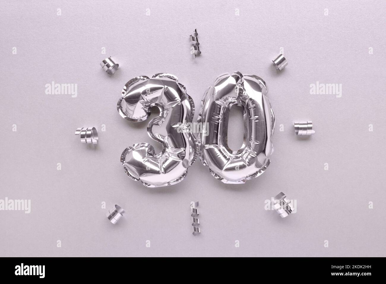 Number thirty inflatable balloons with ribbons confetti on a silver shiny background. Stock Photo