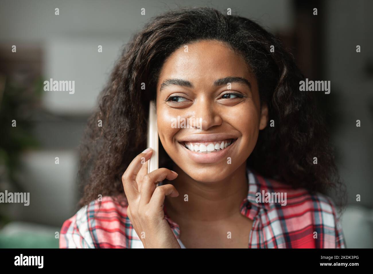 Portrait of cheerful black young woman calling by phone, talking with friend in minimalist living room interior Stock Photo
